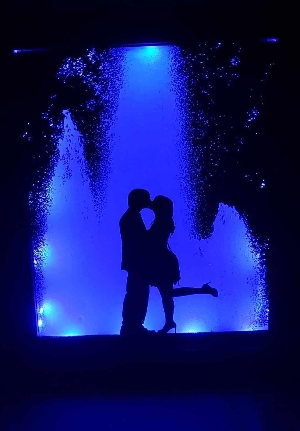 black silhouette of 2 people kissing at a water fountain